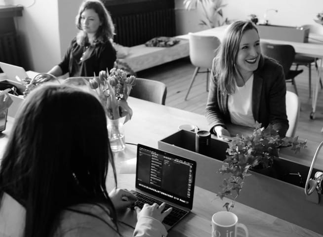 three women working with laptops at the desk and smiling